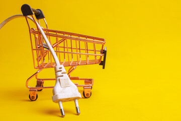 White electrical plug with cable in a shopping cart on a yellow background. Consumption and supply...