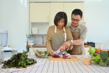 Affectionate senior couple chopping fresh vegetables for salad in cozy kitchen