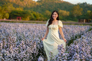beautiful woman in dress enjoying purple marguerite flower blooming in field