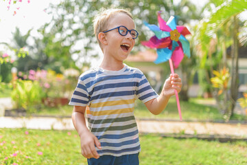 Boy in glasses is playing with pinwheel in a garden