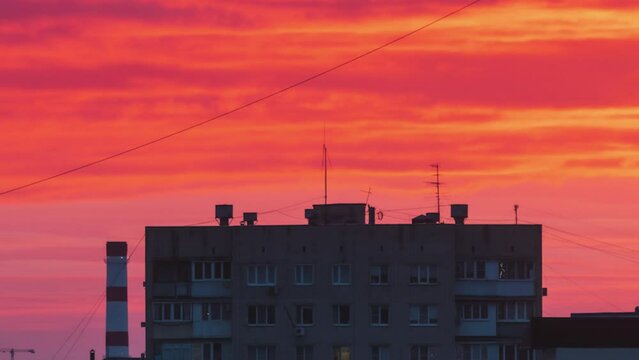 Bright red clouds in a black sky. Time lapse of sunset over the city. Epic fiery clouds. Close-up of a building and a TPP
