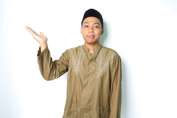 pleased asian muslim man wearing koko clothes presenting to beside with open palm isolated on white...