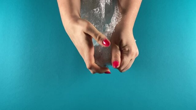 Mental health and well-being concept. Unrecognizable female hands engage in bubble wrap popping for relaxation therapy, stress relief, and calming down. Isolated on a blue background indoors