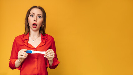 Studio shot of an emotional young woman with a positive pregnancy test in her hands. An expression of bewilderment on his face. The concept of pregnancy, motherhood. A place for your text.