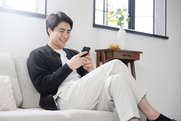 A man in long sleeves relaxing in a clean white living room looking at his phone.