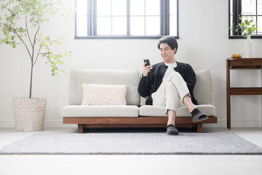 綺麗な白いリビングでスマホを見るくつろぐ長袖の男性 広角