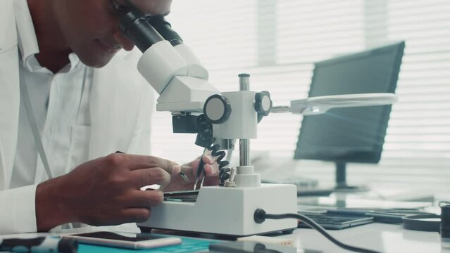 Cropped shot of young Indian man looking at microscope while examining mobile phone breakdown causeCropped shot of young Indian man looking at microscope while examining mobile phone breakdown causeCr