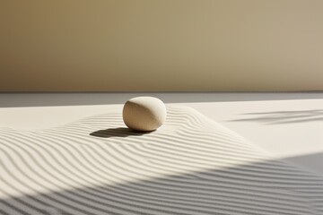 Minimalist composition with a single egg casting a shadow on a textured surface with linear patterns and soft lighting.