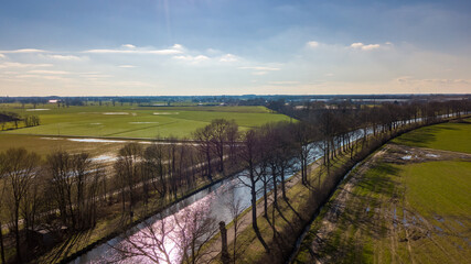 Fototapeta na wymiar This image offers a breathtaking aerial view of a sunlit river meandering gracefully through the countryside. The river reflects the sunlight, creating a striking ribbon of light that contrasts with