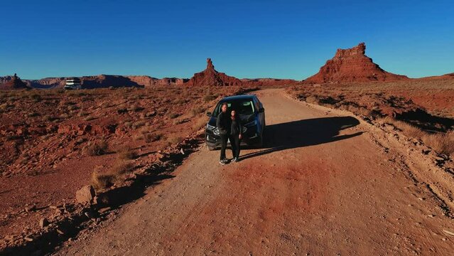 A young couple with their modern car in the red rock desert at Monument Valley in Arizona and Utah.