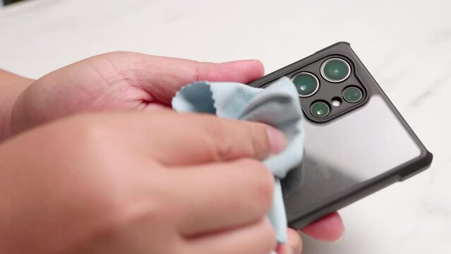 Close-up of a person cleaning up her smart mobile phone with a clean blue washcloth.