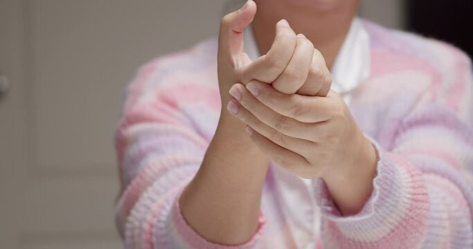 A lady wearing a pink and purple stripes sweater is pinching her hand knuckles and fingers, while massaging herself to relieve them of inflammation and pain.