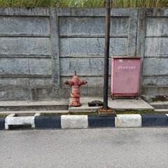 Red fire hydrant in front of a gray wall at a street