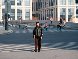 Portrait of handsome Chinese young man with black leather jacket posing with modern city street background in sunny winter day, male fashion, cool Asian young man.