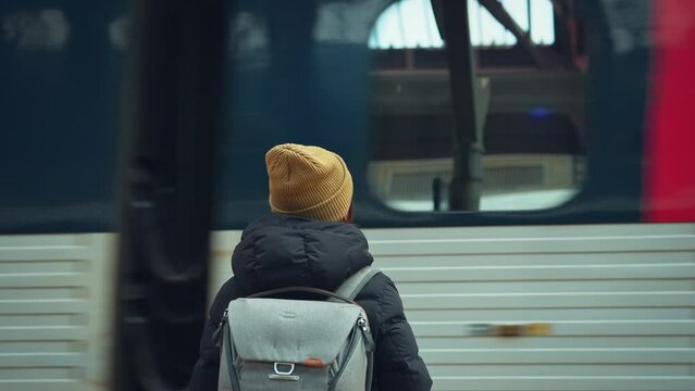 Rear view of young woman with backpack while waiting at platform of train or subway station looking at passing tram, slow motion.
