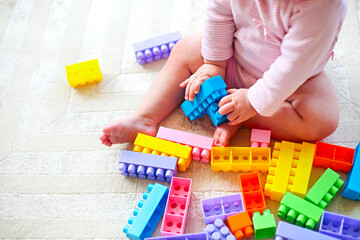 Cute toddler girl having fun with toy blocks sitting on the carpet
