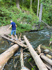 A man crosses a river on fallen logs
