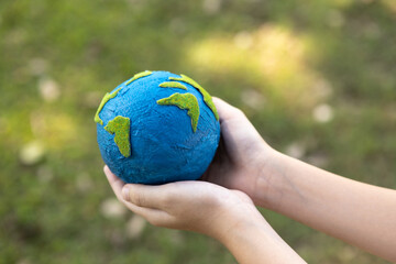 Young boy's hand holding planet Earth globe at natural park background as Earth day to save this planet with ESG principle and environment friendly energy for brighter future. Gyre
