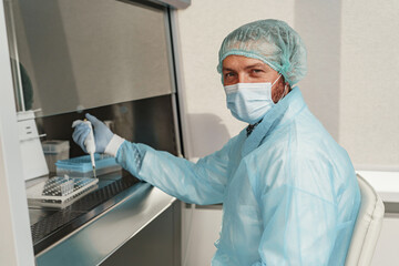 Fototapeta na wymiar Male scientist in mask is using micropipette for biochemical test analysis in medical laboratory