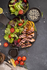 sliced grilled Organic Tuna Steak on black ceramic serving dish with salad on a table