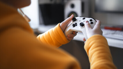 Teenage girl with headset is sitting in a comfortable computer chair, holding a white gamepad in...