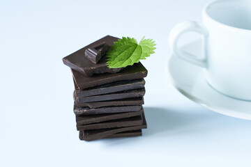 Stack of dark chocolate with mint leaves and cup of coffee on white background