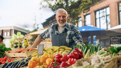 Fototapeta premium Successful Senior Farmer Posing and Cheerfully Smiling for Camera. Middle Aged Bearded Man Selling Farm Produce in His Street Vendor Stall with Sustainable Organic Fruits and Vegetables