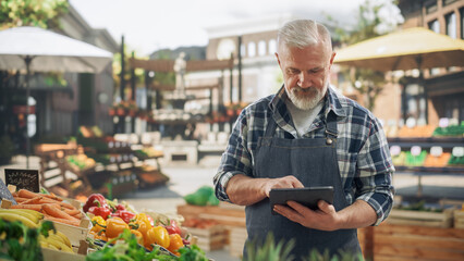 Portrait of an Adult Farmer Using Tablet Computer at Work while Selling Fresh Organic Agricultural Products From a Market Stall. Middle Aged Man Managing Online Orders on an E-Commerce Website