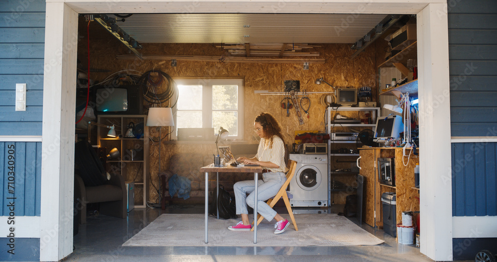Fototapete hispanic female software developer programming on laptop computer in garage at home. focused young w