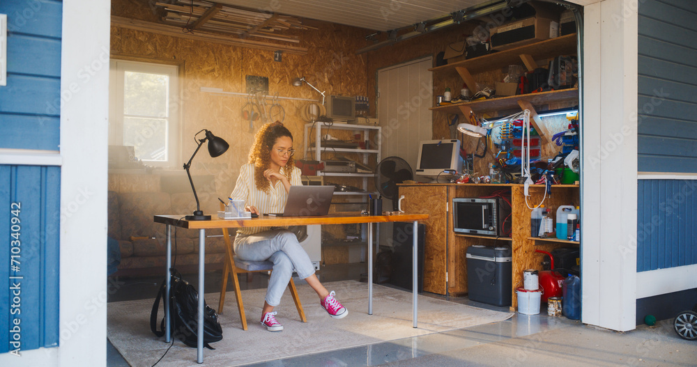Leinwandbilder hispanic female programmer coding on laptop computer in garage at home. young woman working on innov