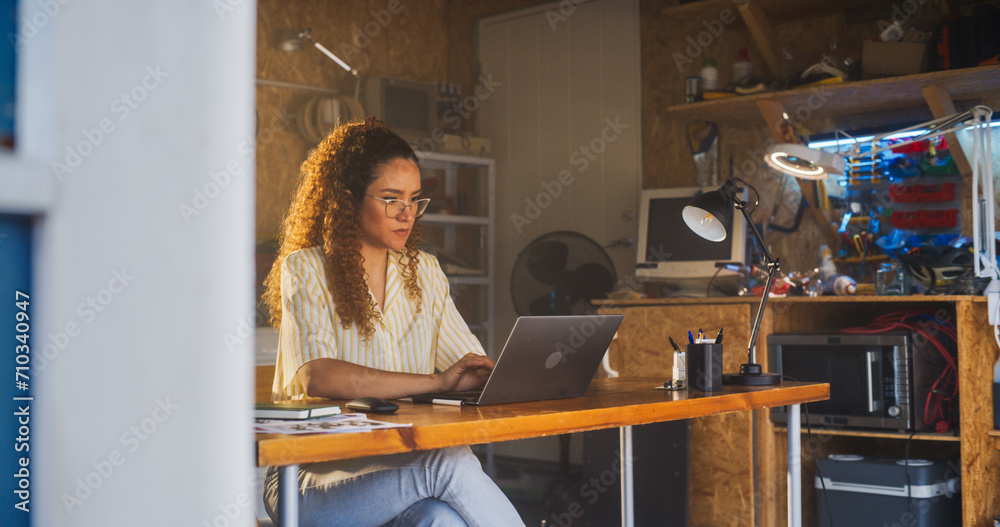 Leinwandbilder hispanic female programmer writing code on laptop computer in garage at home. woman working on innov