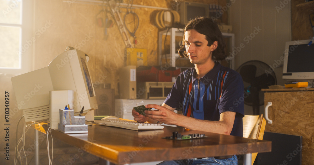 Poster caucasian male computer engineer coding on old desktop pc and inspecting microchip in retro garage. 