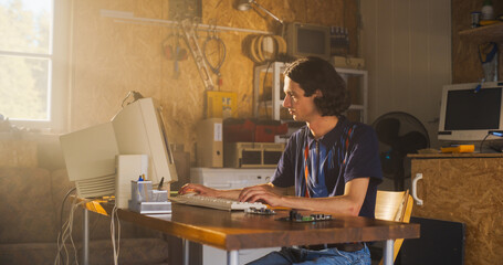 Caucasian Male Computer Engineer Coding On Old Desktop PC And Inspecting Microchip In Retro Garage. Man Starting an Innovative Computer Company In Nineties, Building New Devices. Nostalgia Concept.