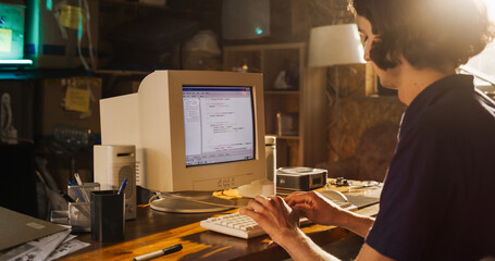 Side View Of Caucasian Male Software Engineer Programming on Old Desktop Computer In Retro Garage. Focused Man Starting Tech Startup Company In Nineties. Coding Innovative Online Service At Home. - obrazy, fototapety, plakaty
