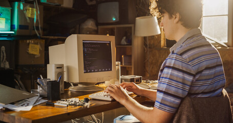 Caucasian Male Computer Engineer Programming On Old Desktop Computer In Retro Garage. Experienced Software Developer Writing Code For New Innovative Portable Device Startup In Nostalgic Nineties.