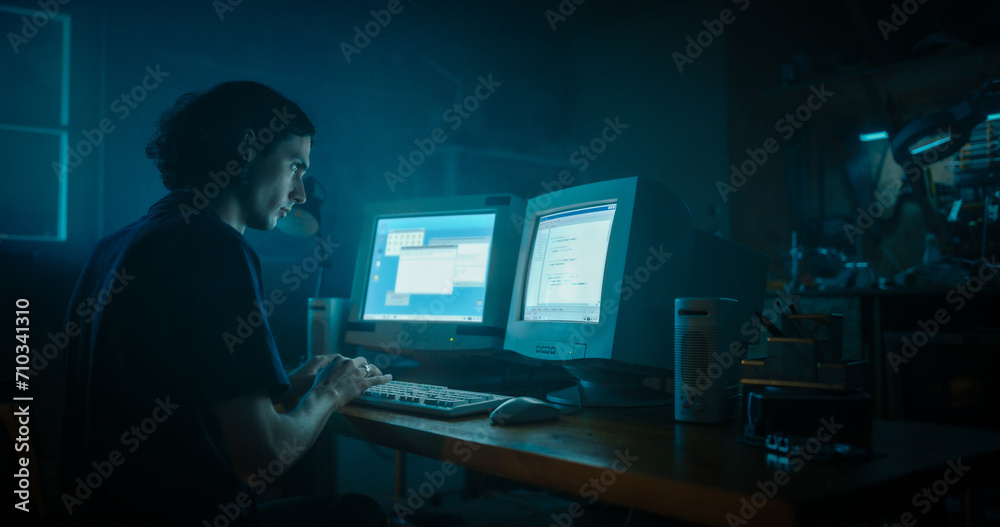 Poster Caucasian Male Programmer Using Old Desktop Computer With Two Monitors In Retro Garage Late At Night. Evil Hacker Searching For Software Vulnerabilities, Coding DDOS Attack, Trojan Horse Program.