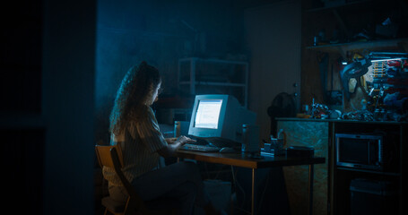 Hispanic Female Programmer Using Old Desktop Computer In Retro Garage Late At Night. White Hat...