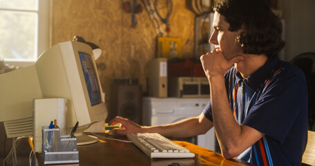Portrait Of Caucasian Male Software Engineer Programming on Old Desktop Computer In Retro Garage In...
