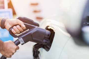 Concepts about using electric cars. Close up an electric car user is holding a black charger to recharge an electric car. The use of electric cars as the latest alternative energy source in Thailand.