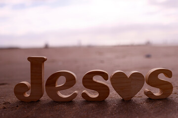 Wooden letters forming the word Jesus  on a background of beach sand. Christian symbol.