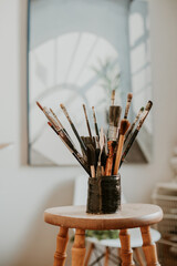 a collection of paintbrushes on a wooden stool in the art studio