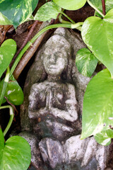 Small Buddha statue on a rock with green leaves.. Phnom Penh; Cambodia.