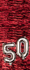 Silver foil balloon number number 50 on a background of red tinsel decoration. Birthday greeting...