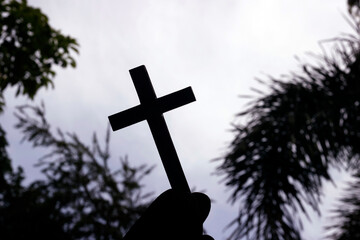Man holding a christian cross against the sky. Religious symbol of christianism.