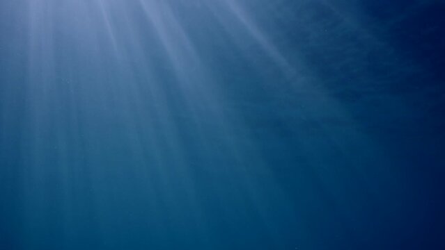 Underwater sunrays in blue Ocean, Slow motion. The sun's rays penetrate underwater into blue water through sea surface. Diagonal sunbeams under water. 