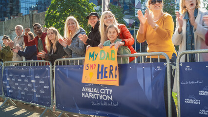 Diverse Group of People Running a Marathon in a City During the Day. Supportive Family Members in...