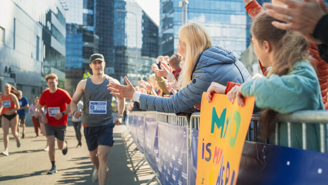 Marathon Audience Supporting and Cheering Their Loved Ones Participating in the Race: Athletic Male Marathon Runner Giving a High Five to Female Family Member in the Audience While Running
