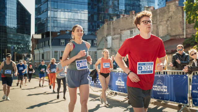 Group of Diverse People Running in a Marathon with the Cheers of their Loved Ones and Supporters in the Audience. Runners Participating in a Charity Run to Raise Money a Cause - Powered by Adobe