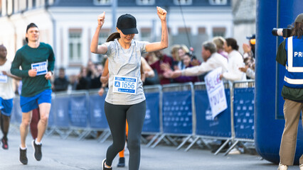 Portrait of Happy Female Runner Participating in a Marathon. Athletic Female Crossing the Finish Line, Celebrating, Raising Hands in the Air