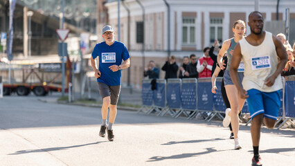 Portrait of a Senior Male Jogger Running in a City Marathon and Being Cheered for by the Audience....